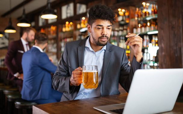 People and bad habits concept. Business man drinking beer and smoking cigarette at pub - Foto, Imagen