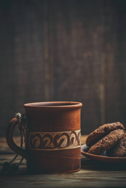 Brown clay vintage coffee mugs and delicious chocolate chip cookies on a wooden table in warm colors - Fotografie, Obrázek
