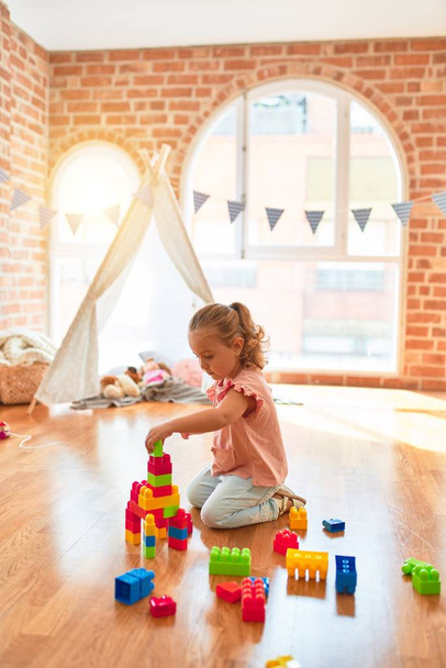 Piękna blondynka maluch dziewczyna gra z bloków plastikowych do budowy wieży w przedszkolu - Zdjęcie, obraz