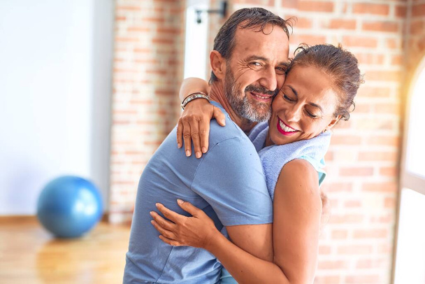 Edad media hermosa pareja deportiva sonriendo feliz. De pie con sonrisa en la cara abrazándose en el gimnasio
 - Foto, imagen