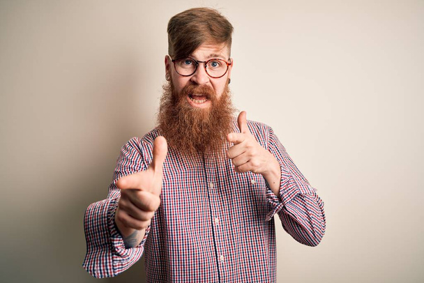 Beau rouquin irlandais homme d'affaires avec barbe portant des lunettes sur fond isolé pointant les doigts vers la caméra avec un visage heureux et drôle. Bonne énergie et vibes
. - Photo, image