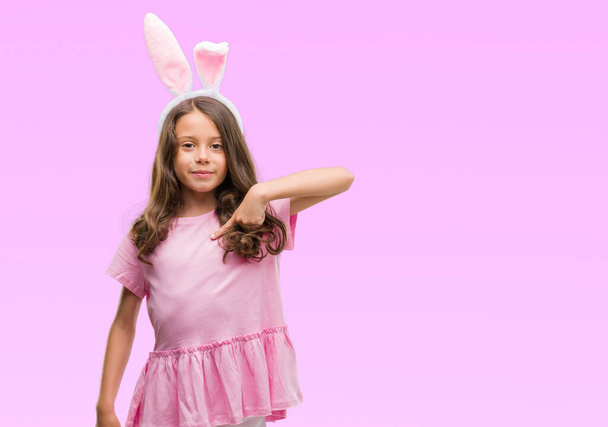 Bruna ragazza ispanica indossa orecchie di coniglio pasquale con faccia a sorpresa puntando il dito verso se stesso
 - Foto, immagini