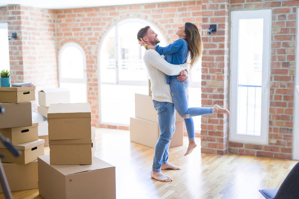 Young beautiful couple at new home around cardboard boxes - Fotografie, Obrázek