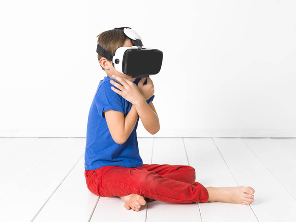 cool and beautiful boy with red trousers and blue shirt is using virtual 3d glasses at home and is having fun - Photo, Image
