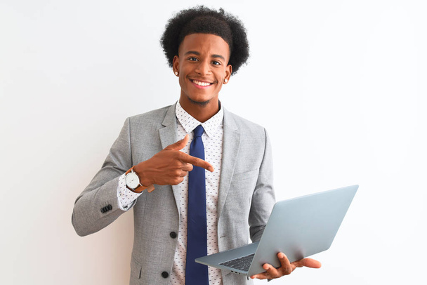 Молодой африканский американский бизнесмен, использующий ноутбук, стоящий на изолированном белом фоне, очень доволен, указывая рукой и пальцем
 - Фото, изображение