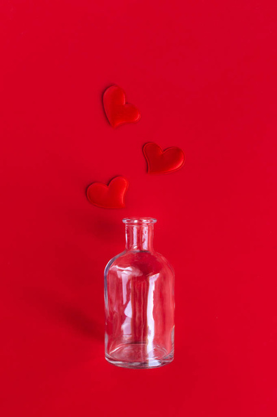 Bottle with red hearts on red background. Minimal concept for Valentine day. - Фото, изображение