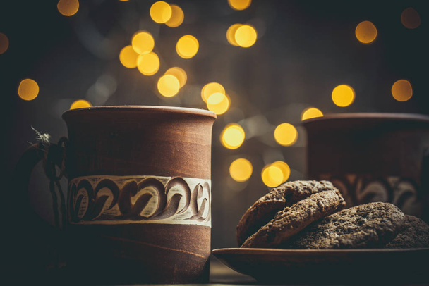 Brown clay vintage coffee mugs and delicious chocolate chip cookies on a wooden table in warm colors - Zdjęcie, obraz