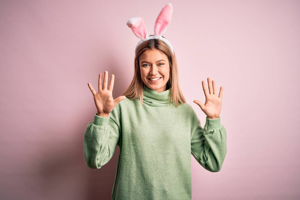 Молода красива жінка в великодніх вухах кролика стоїть над ізольованим рожевим тлом, показуючи і вказуючи пальцями номером десять, посміхаючись впевнено і щасливо
. - Фото, зображення