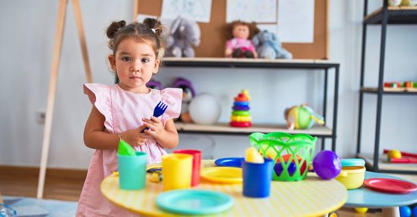 Mladý krásný batole hrát s příbory a jídlo hračky na stole ve školce - Fotografie, Obrázek