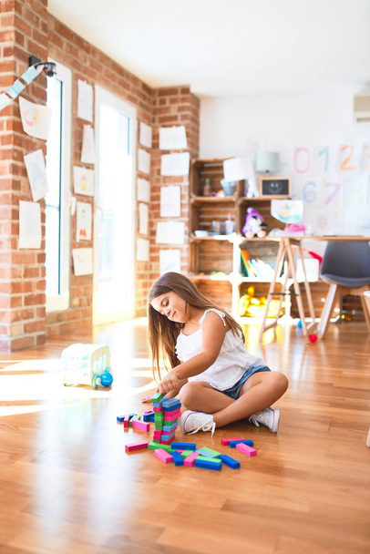 entzückendes Kleinkind, das auf dem Boden sitzt. Spielen mit Holzbausteinen im Kindergarten - Foto, Bild