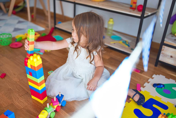 Adorabile bambino biondo che gioca con i blocchi di costruzione intorno a un sacco di giocattoli all'asilo
 - Foto, immagini