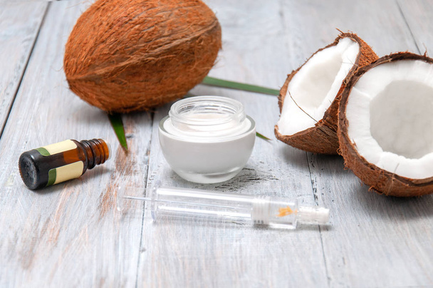 Coconut halved, essential oil in a glass bottle and cream on a gray wooden table. Personal care. Spa treatments. Cosmetology. Natural and organic cosmetics. - Photo, Image