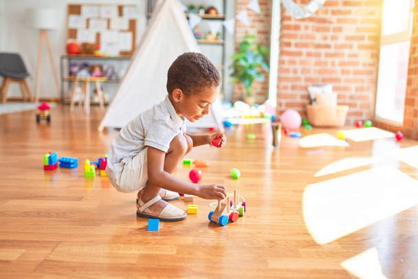 Красивый африканский американский ребенок играет с деревянными блоками поезд игрушки вокруг много игрушек в детском саду
 - Фото, изображение