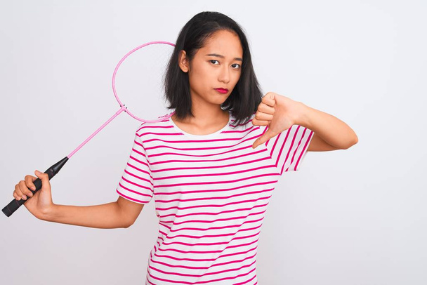Young beautiful chinese woman holding badminton racket over isolated white background with angry face, negative sign showing dislike with thumbs down, rejection concept - Φωτογραφία, εικόνα