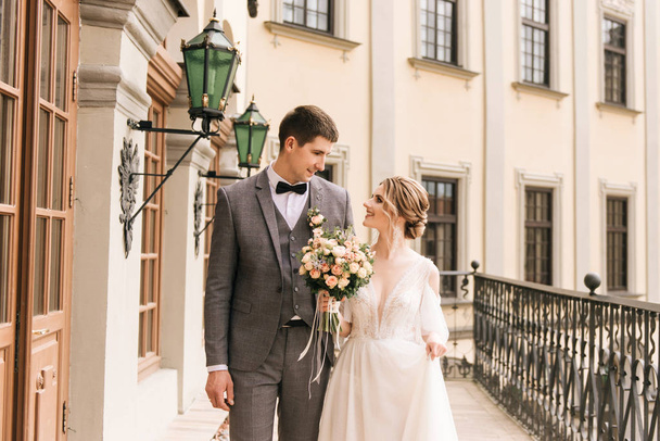 Beautiful elegant couple of newlyweds in love on the background of an old building and paving stones, European wedding - Фото, изображение