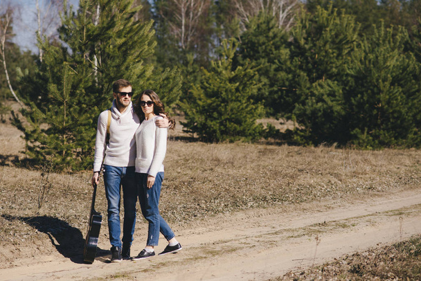 Chica feliz y chico con mochila turística y guitarra caminando en la naturaleza, viaje concepto de historia de amor, enfoque selectivo
 - Foto, Imagen