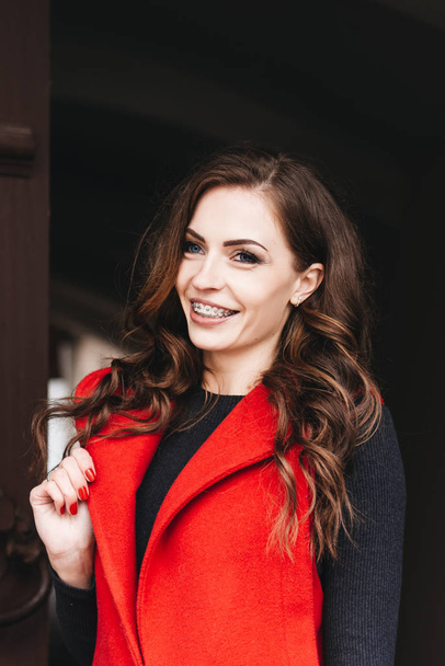 Outdoor portrait of a stylish young girl on the street of an old city in black clothes and a long red vest. A model poses on the street of a European city - Фото, зображення