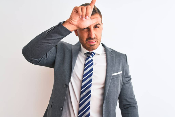 Young handsome business man wearing suit and tie over isolated background making fun of people with fingers on forehead doing loser gesture mocking and insulting. - Photo, Image