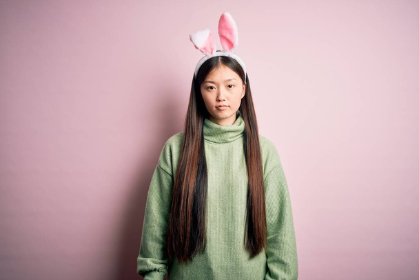 Young asian woman wearing cute easter bunny ears over pink background Relaxed with serious expression on face. Simple and natural looking at the camera. - Photo, Image