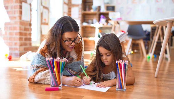 Bella insegnante e bambino disegno utilizzando matite e carta intorno a un sacco di giocattoli all'asilo
 - Foto, immagini