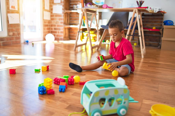 Чарівний малюк грає з будівельними блоками навколо безлічі іграшок в дитячому саду
 - Фото, зображення