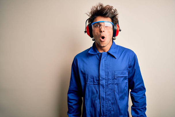 Young constructor man wearing uniform and earmuffs over isolated white background afraid and shocked with surprise expression, fear and excited face. - Foto, immagini
