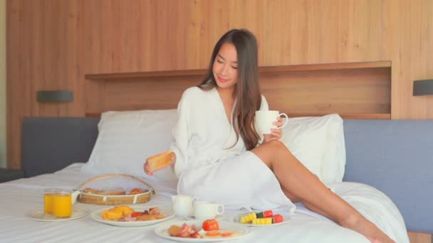 Güzel Asyalı kadının evde yatakta kahvaltı yaparken kahve içtiği görüntüler. - Video, Çekim