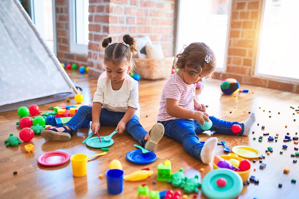 Suloiset pikkulapset, jotka pelaavat aterioita käyttämällä muovista ruokaa ja ruokailuvälineitä lelu päiväkodissa
 - Valokuva, kuva