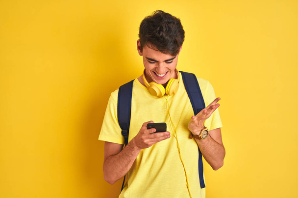 Teenager boy wearing headphones and using smartphone over isolated background very happy and excited, winner expression celebrating victory screaming with big smile and raised hands - Foto, Imagen