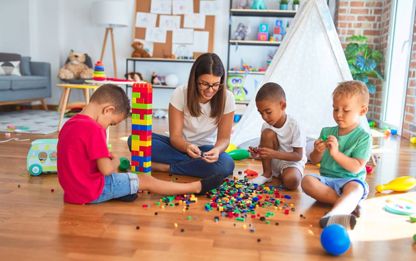 Junge schöne Lehrerin und Kleinkinder spielen im Kindergarten mit Bauklötzen um viele Spielsachen - Foto, Bild