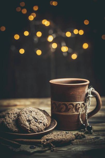 Brown clay vintage coffee mugs and delicious chocolate chip cookies on a wooden table in warm colors - 写真・画像