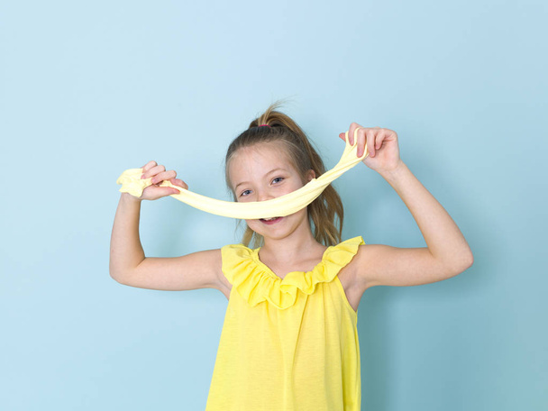 beautiful 9 year old girl is playing with yellow slime in front of blue background - Fotoğraf, Görsel