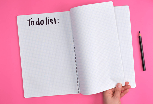 empty open notebook in a cell and a female hand, pink background, to do list - Fotografie, Obrázek