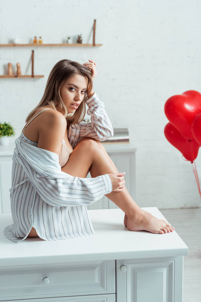sexy woman sitting on table near red heart-shaped balloons  - Фото, изображение