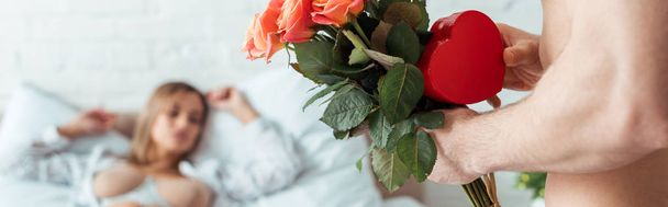 panoramic shot of man with flowers and heart-shaped gift near seductive woman  - Фото, изображение