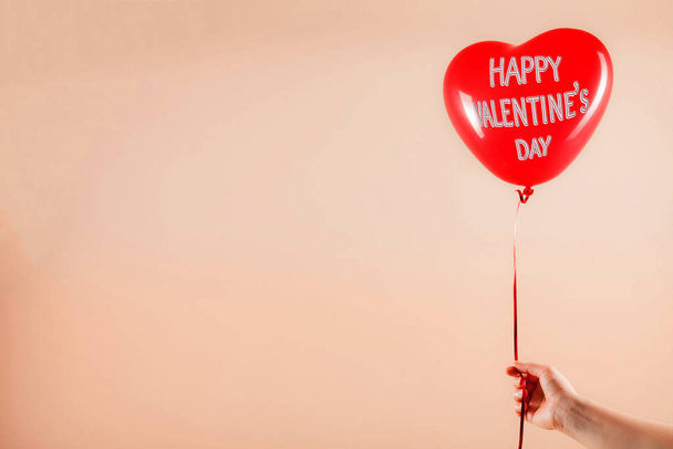 Vrouwelijke hand houdt rood rubber opblaasbare hartvorm ballon. Liefde, relatie, Valentijnsdag en verjaardagsfeest concept. Studio shot op een abstracte wazige achtergrond met lege kopieerruimte - Foto, afbeelding