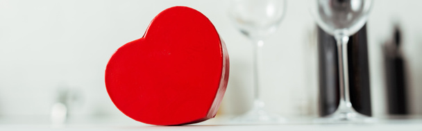 colpo panoramico di scatola regalo a forma di cuore rosso vicino a bicchieri vuoti
  - Foto, immagini