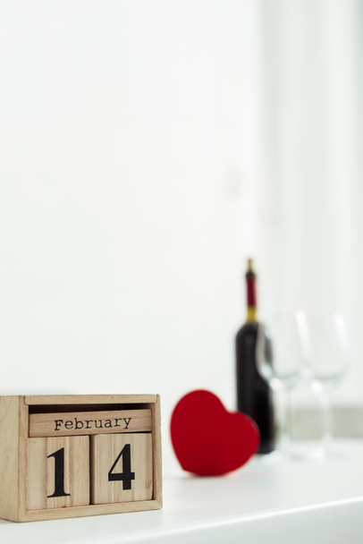 selective focus of wooden cubes with 14 february lettering near bottle of wine and glasses  - Foto, Imagen