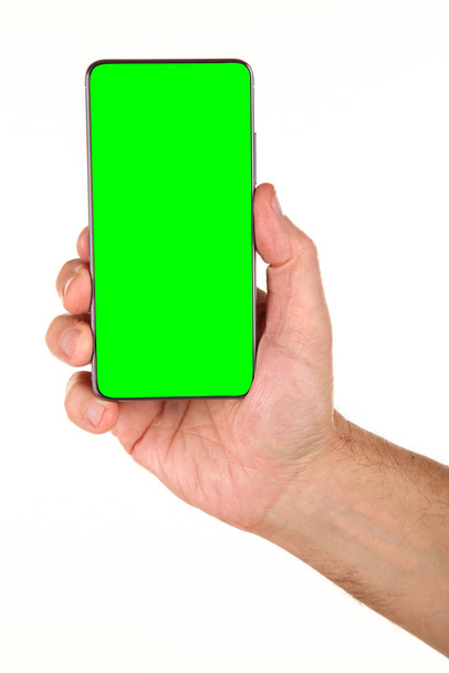Human hand holds a modern smartphone with a blank chromakey screen in a palm. Technology and advertising concept. Detailed closeup studio shot isolated on abstract blurred white background - Фото, изображение