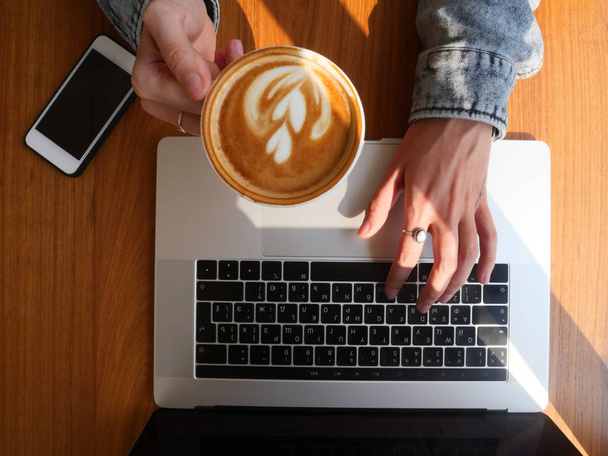 Top view tattooed girl hands texting on laptop holding coffee cup - Foto, afbeelding