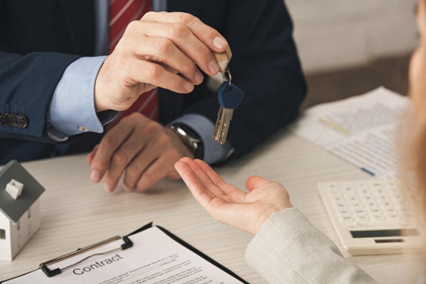 cropped view of realtor giving keys to woman with cupped hand near contract  - Photo, Image
