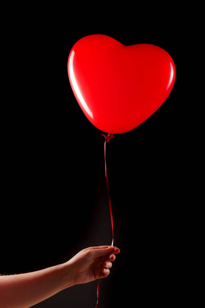 Female hand holds red rubber inflatable heart shape balloon. Love, relationship, valentines day and birthday celebration concept. Studio shot on an abstract blurred background with blank copy space - 写真・画像