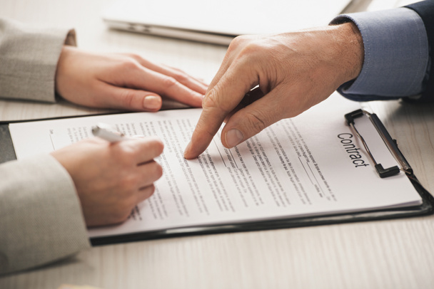 cropped view of realtor pointing with finger at clipboard with contract lettering near woman  - Photo, Image