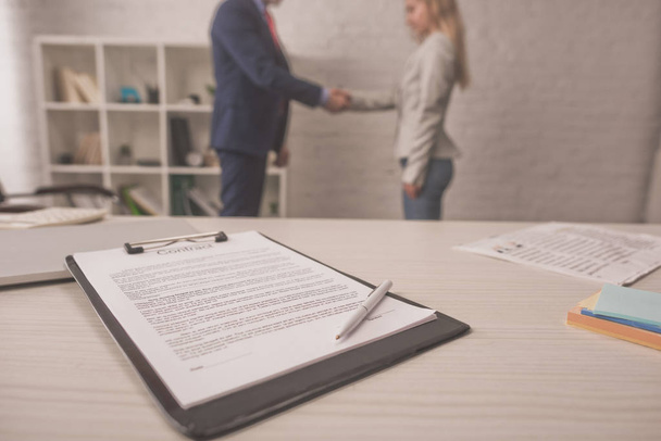 selective focus of clipboard with document on table near agent and client shaking hands - Photo, Image