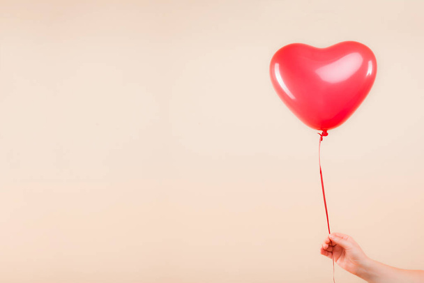 Female hand holds red rubber inflatable heart shape balloon. Love, relationship, valentines day and birthday celebration concept. Studio shot on an abstract blurred background with blank copy space - Fotoğraf, Görsel