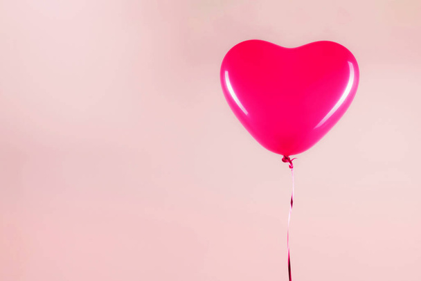 Female hand holds pink rubber inflatable heart shape balloon. Love, relationship, valentines day and birthday celebration concept. Studio shot on an abstract blurred background with blank copy space - Zdjęcie, obraz