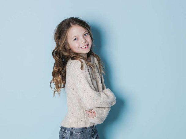 pretty and cool 9 year old girl with brown wool sweater posing in front of blue background in the studio - Фото, зображення