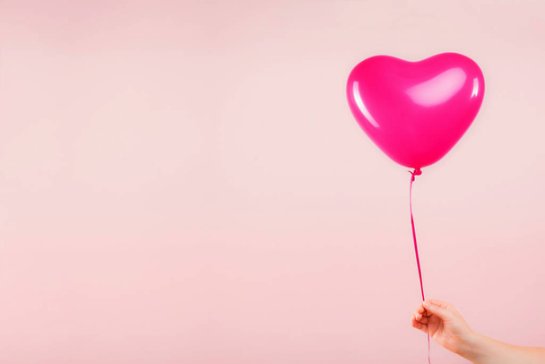 Female hand holds pink rubber inflatable heart shape balloon. Love, relationship, valentines day and birthday celebration concept. Studio shot on an abstract blurred background with blank copy space - Фото, изображение