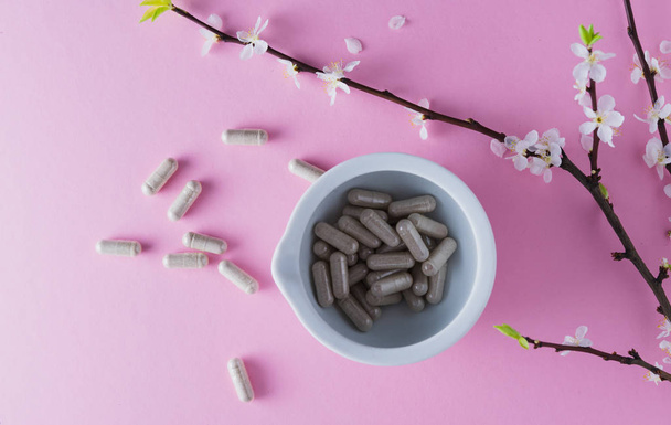 Gray capsules in a medical mortar and flowering apricot branch on a pink background - Photo, Image
