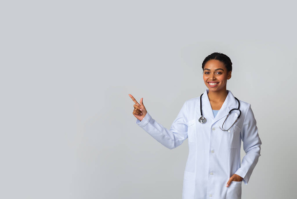 młody czarny kobieta lekarz wskazując na ksero przestrzeń na lekkim tle - Zdjęcie, obraz